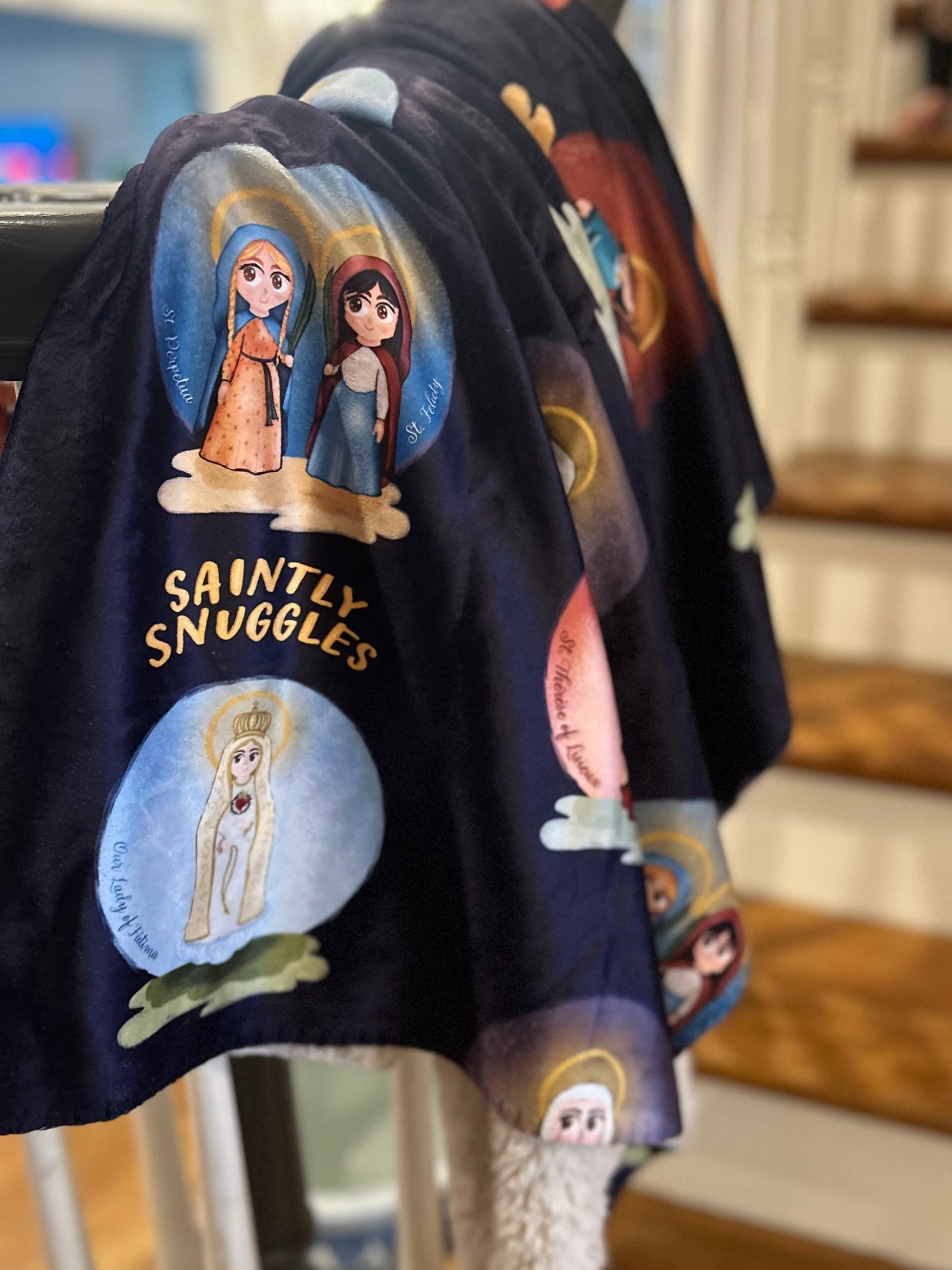Navy blue shirt with cartoon designs and text 'Saintly Snuggles' hanging on a rack.
