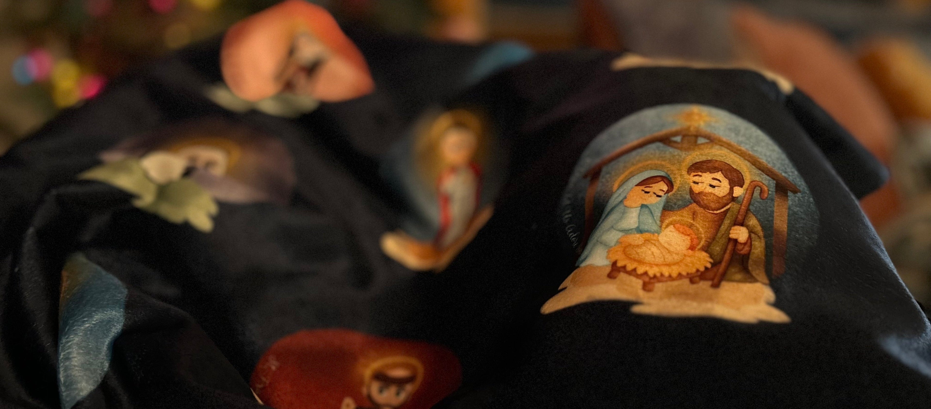 Dark fabric with nativity scene prints in front of a blurred Christmas tree.