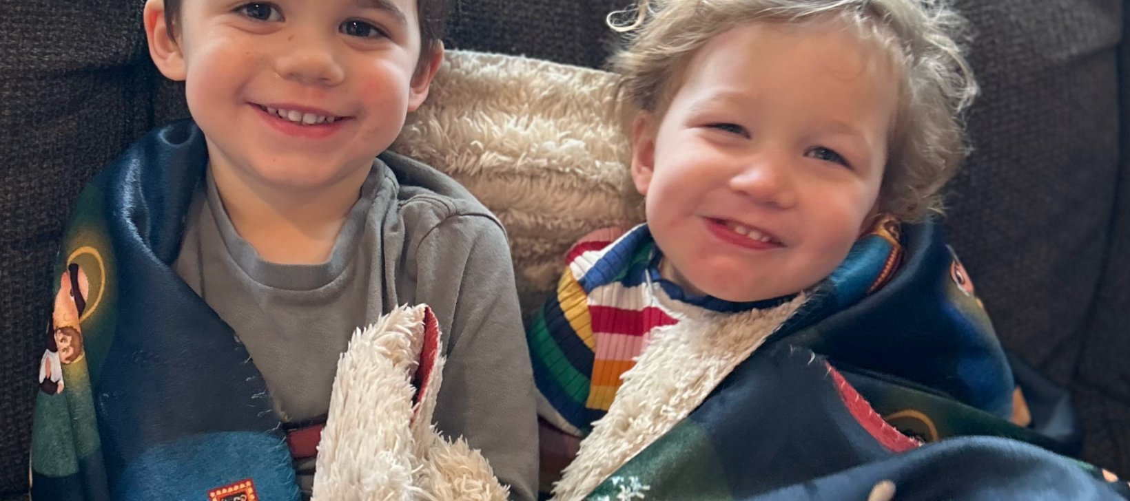 Two children wrapped in a blanket with colorful designs, sitting together.